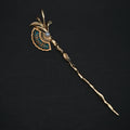 A vintage gold hairpin with a decorative fan-shaped enamel inlay, a central pearl-like bead, and a long twisted stem, displayed on a dark background.